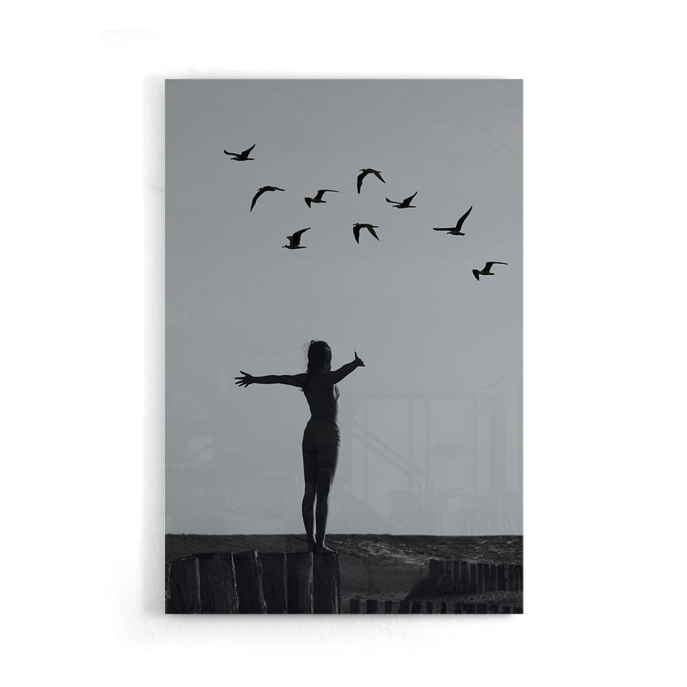Zwart-wit fotografie van een vrouw op een rots met vogels luxe glasschilderij op groot formaat